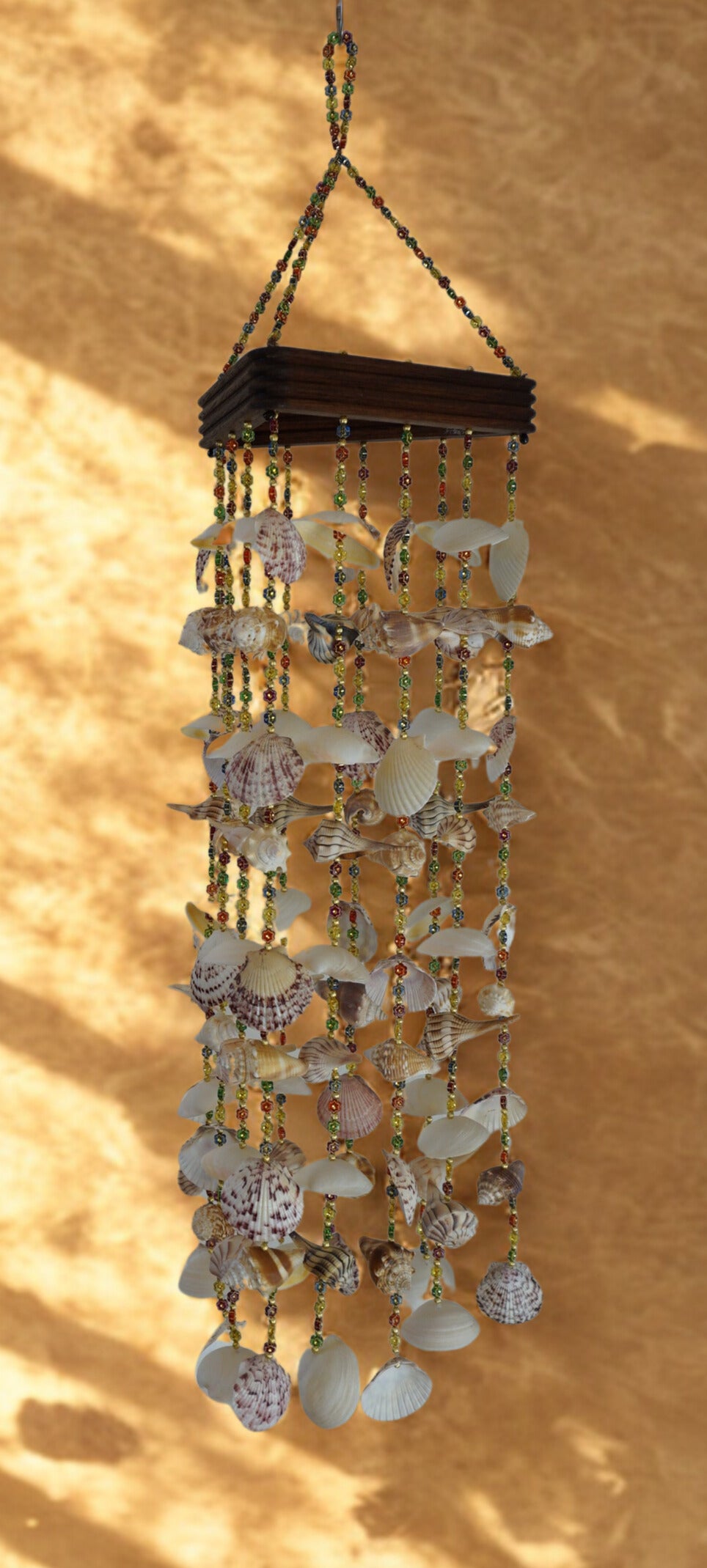 Decorative shell wind chime hanging against a textured beige wall.
