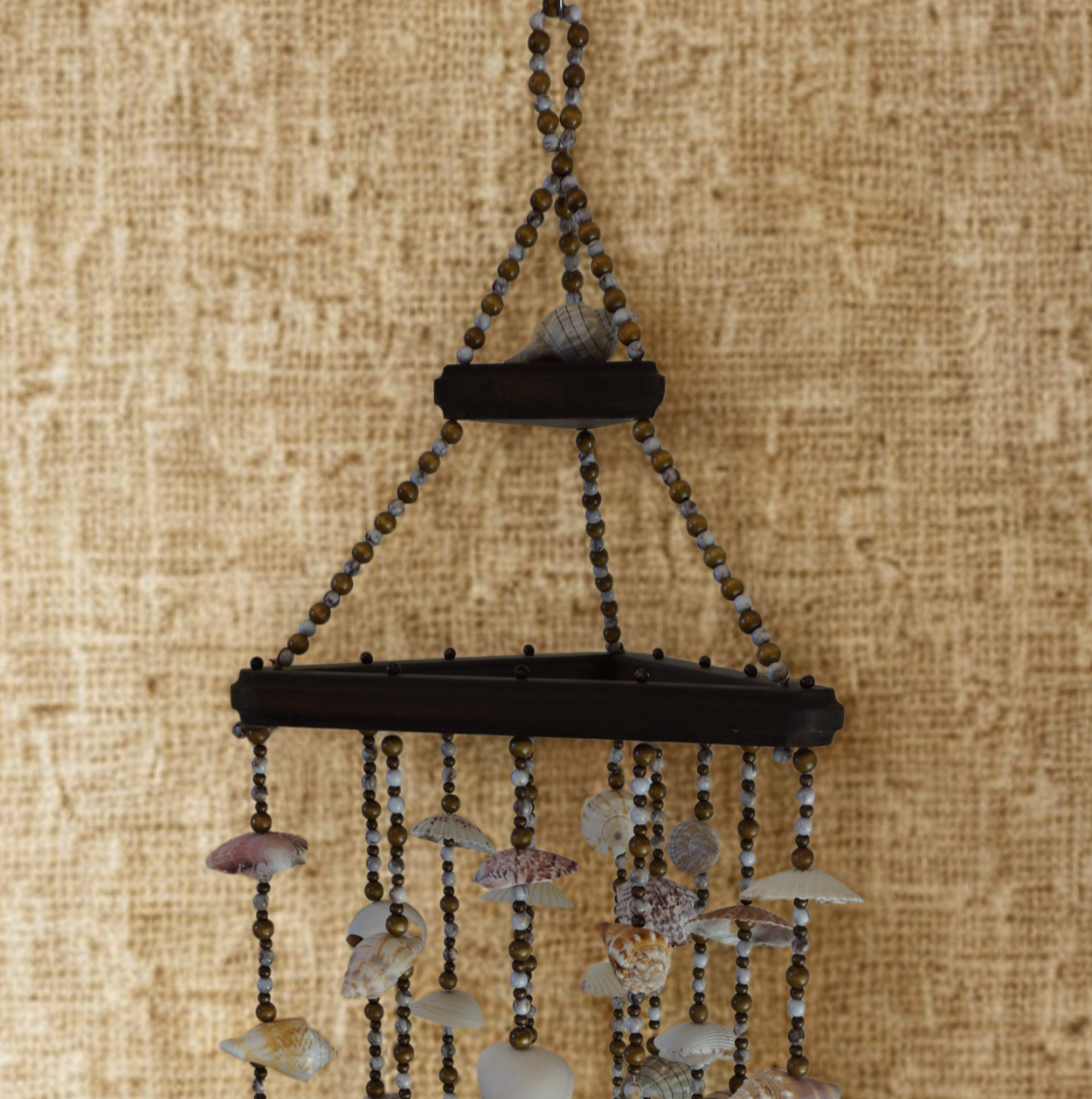 Decorative wind chime with seashells and beads on a textured beige background