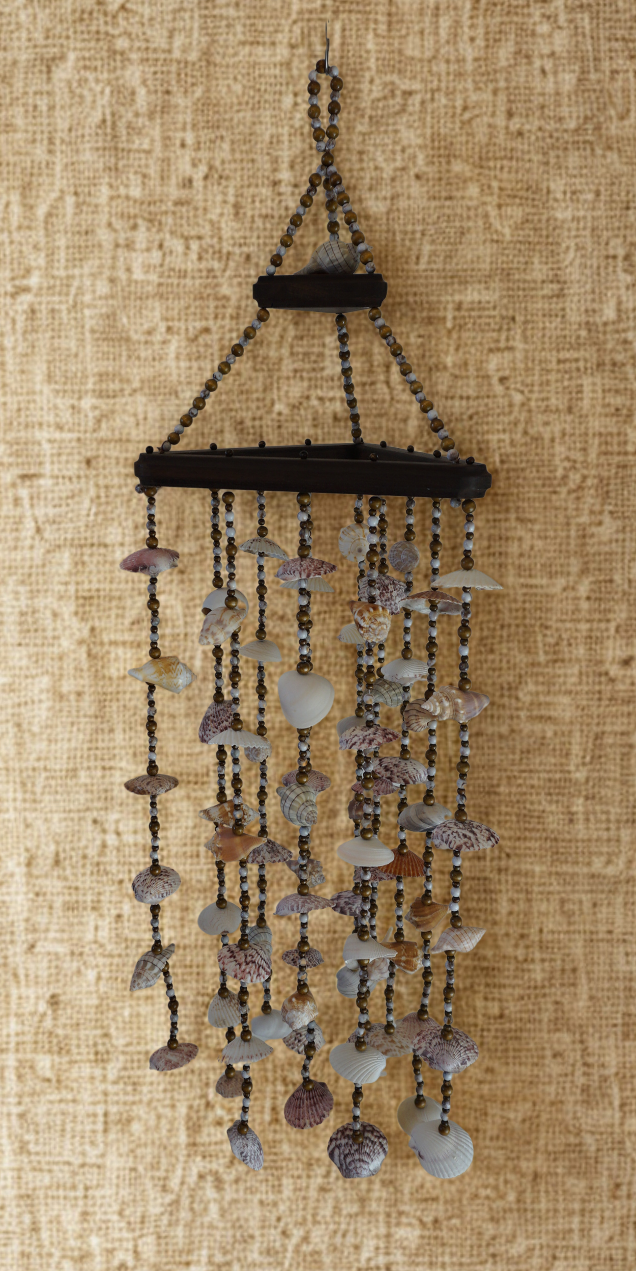 Decorative shell wind chime hanging against a textured beige background