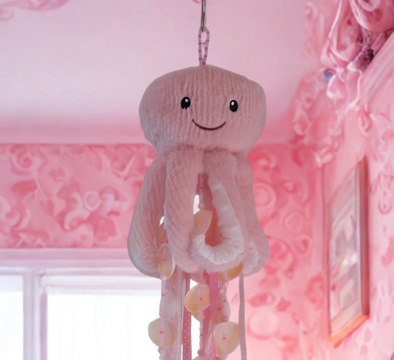 Decorative plush octopus wind chime with shells hanging in a pink-themed room