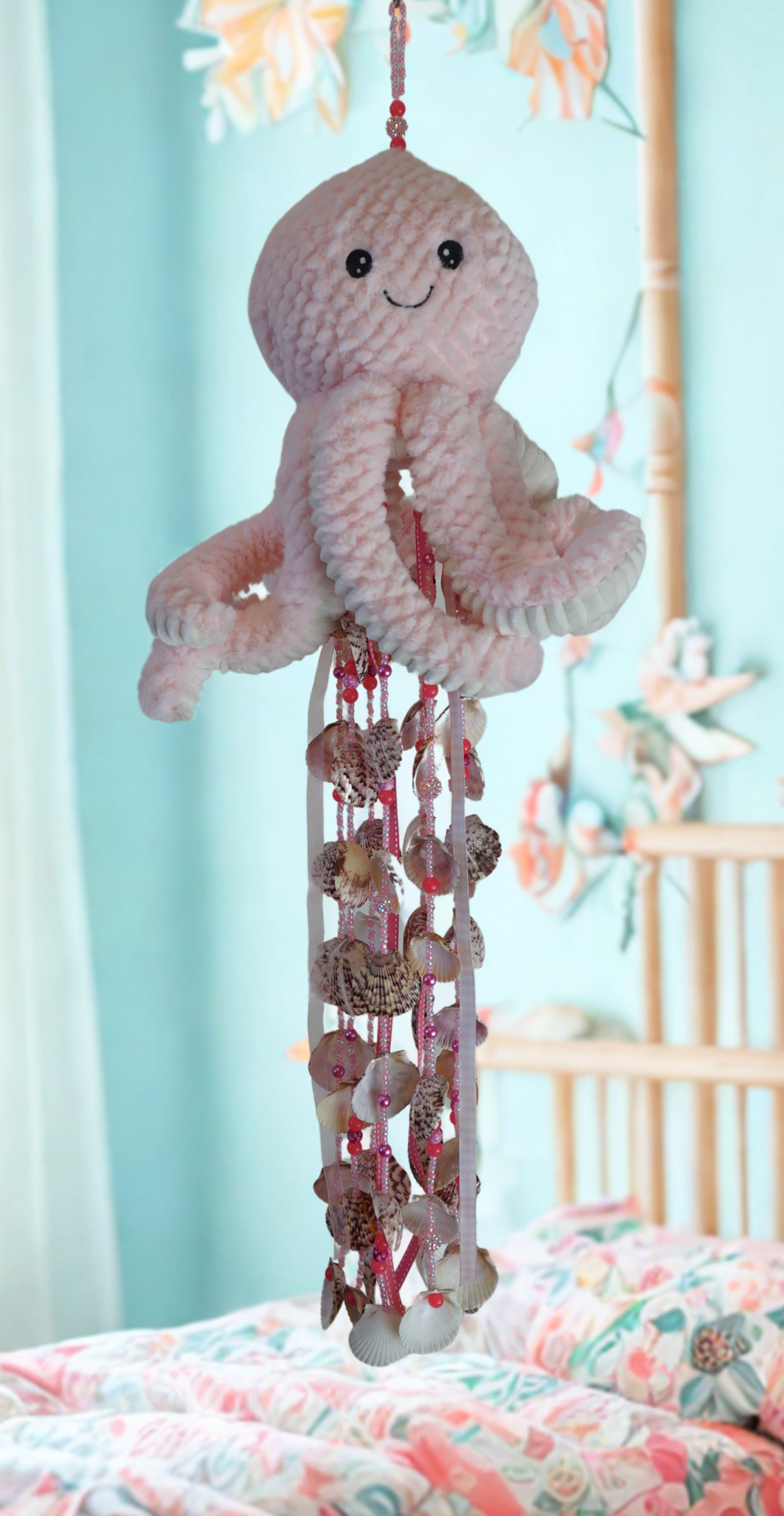 Plush octopus wind chime with decorative shells hanging above a crib with a colorful blanket.