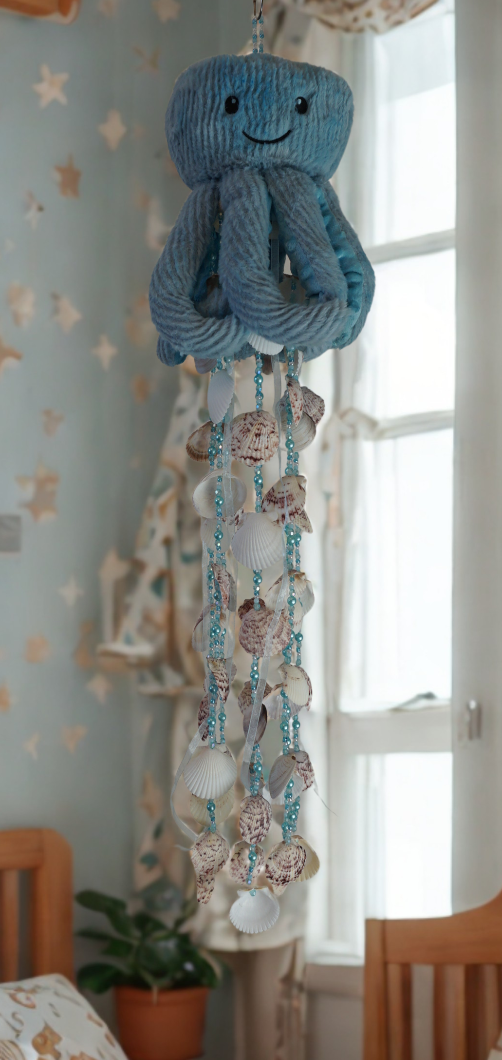 Decorative wind chime octopus with seashells hanging in a room with a window and plant.