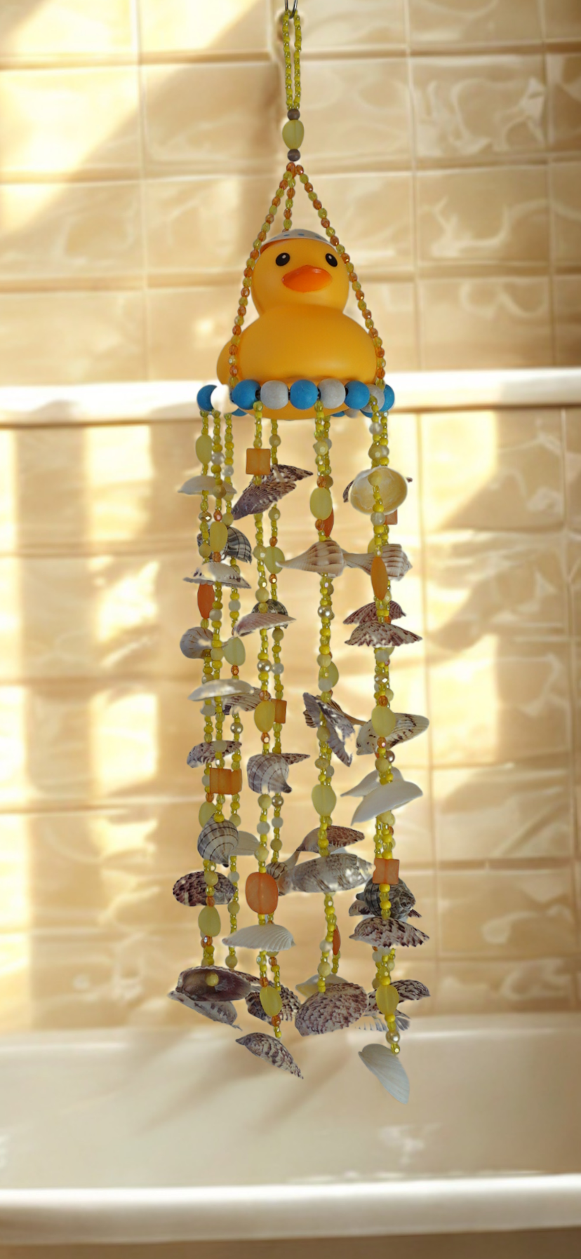 Decorative wind chime with a rubber duck on top and shells hanging against a tiled wall.