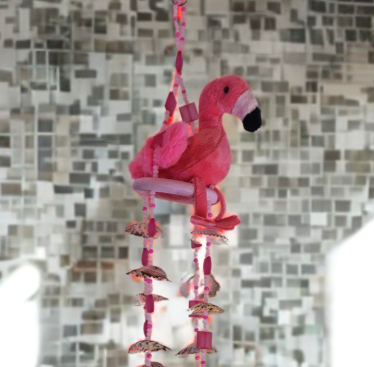 Pink flamingo wind chime with shells against a mosaic tile wall.