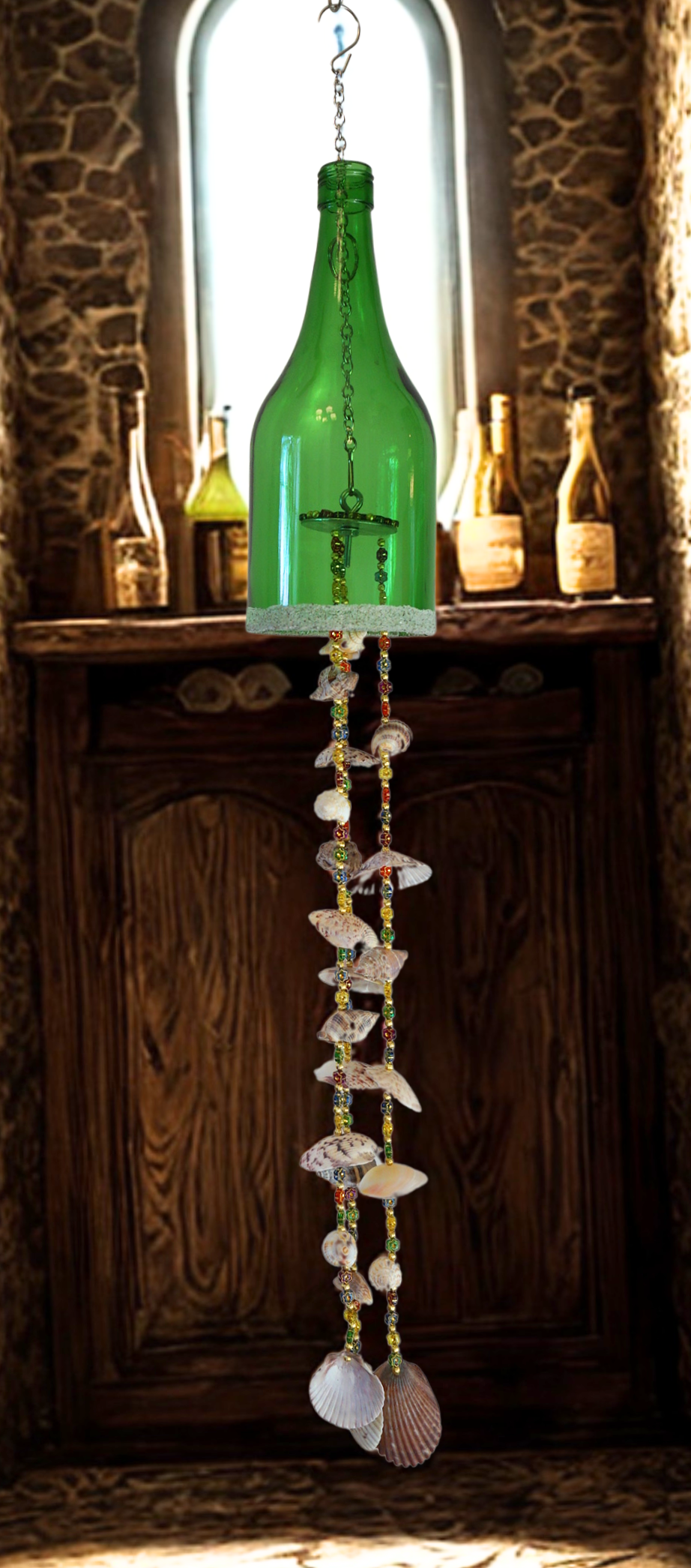 Decorative hanging bottle wind chime with seashells against a rustic stone wall.