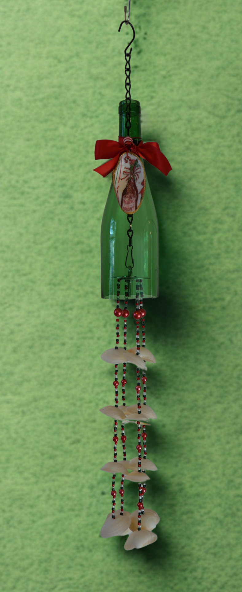 Decorative hanging bottle wind chime with shells and beads on a green background