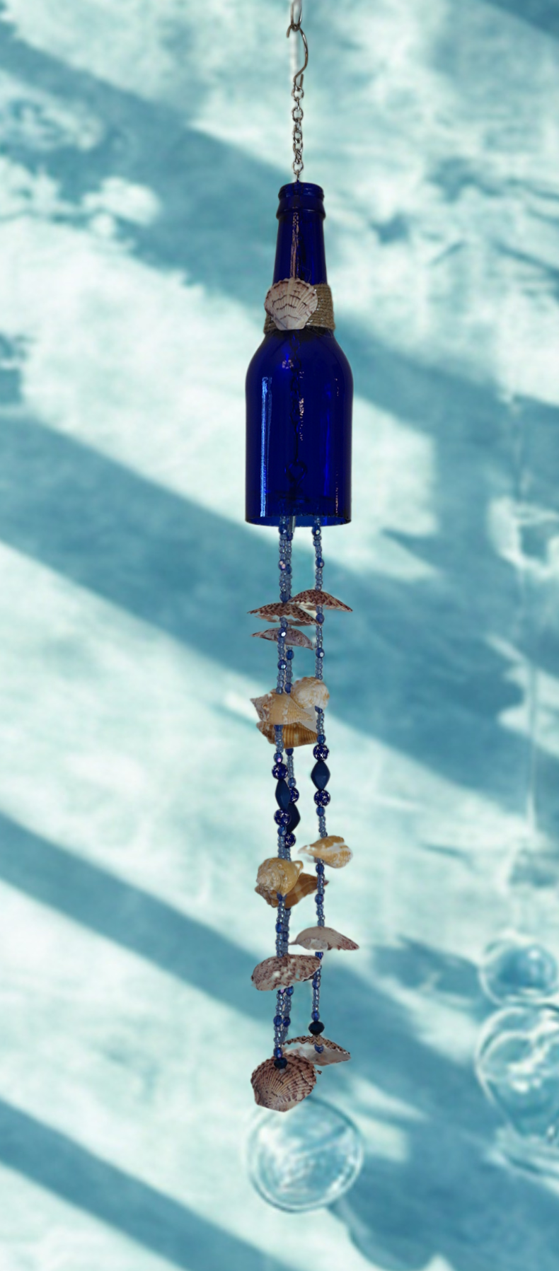 Blue glass bottle wind chime with decorative shell elements against a light blue background