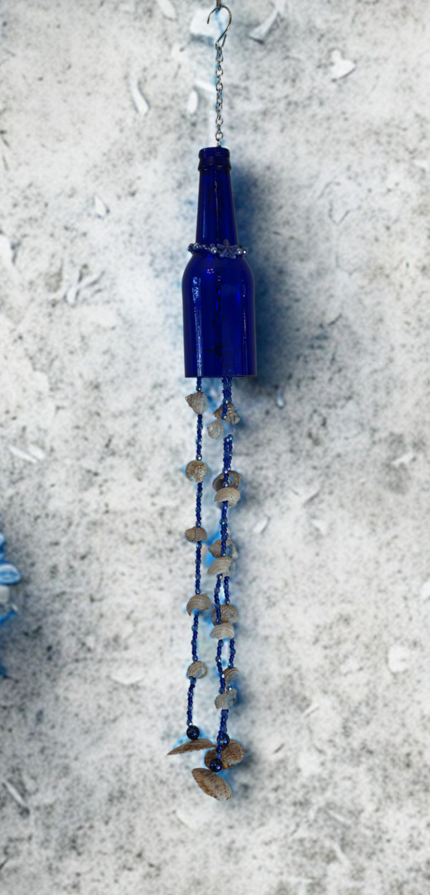 Blue bottle wind chime with decorative shell elements on a textured surface