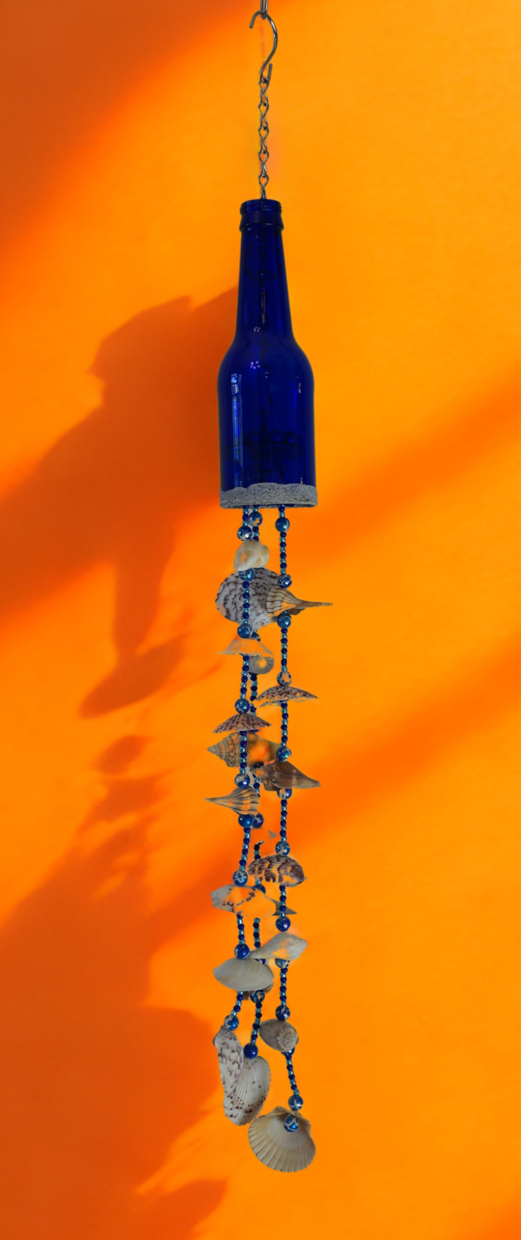 Blue bottle wind chime with decorative shell elements on an orange background