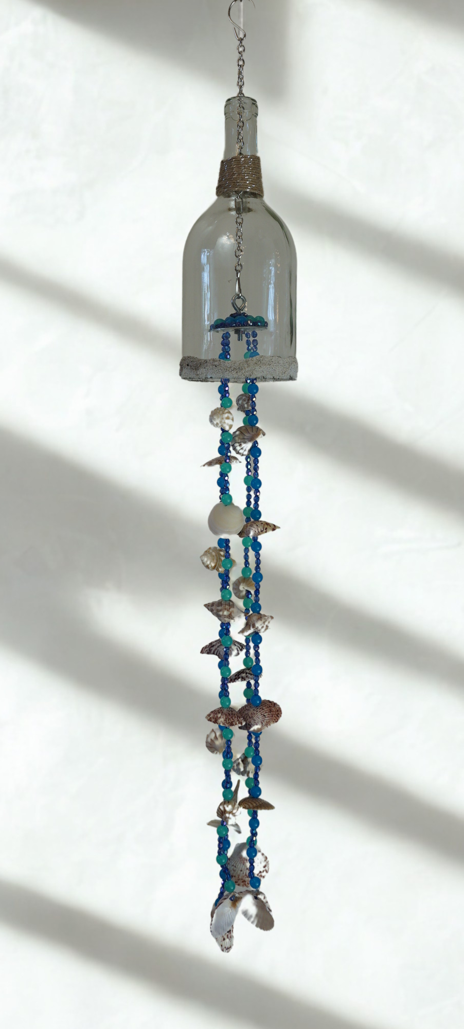 Decorative hanging wind chime with glass bottle, shells and beads on a white background