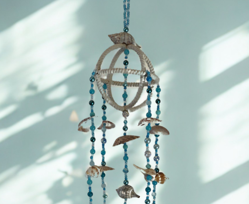 Decorative hanging wind chime with blue beads and shells against a light blue wall.