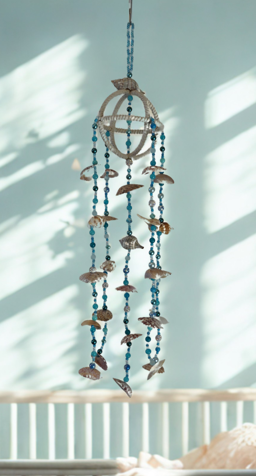Decorative hanging mobile with blue beads and shells against a light blue wall.