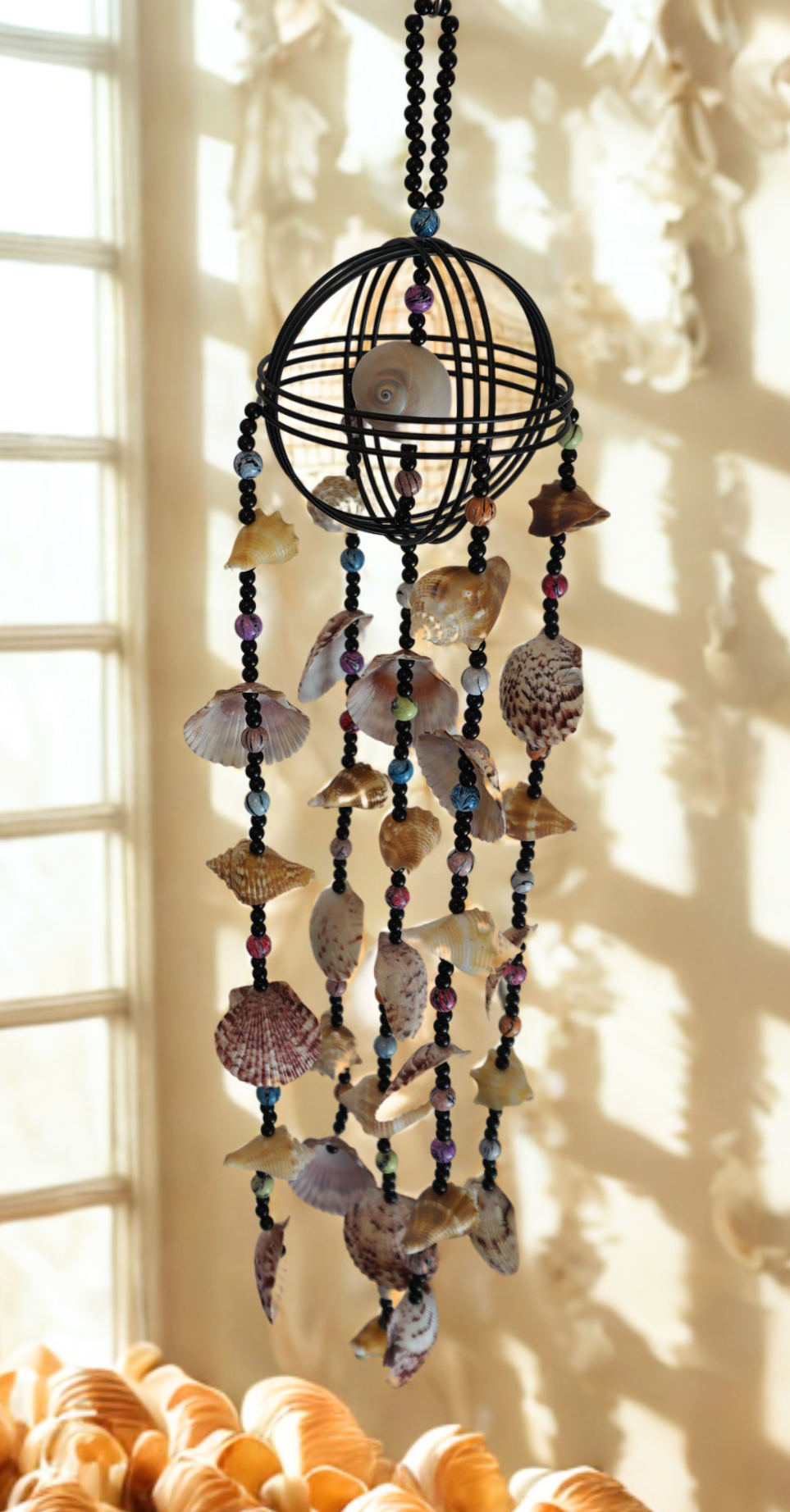 Decorative shell and bead wind chime hanging in front of a window.