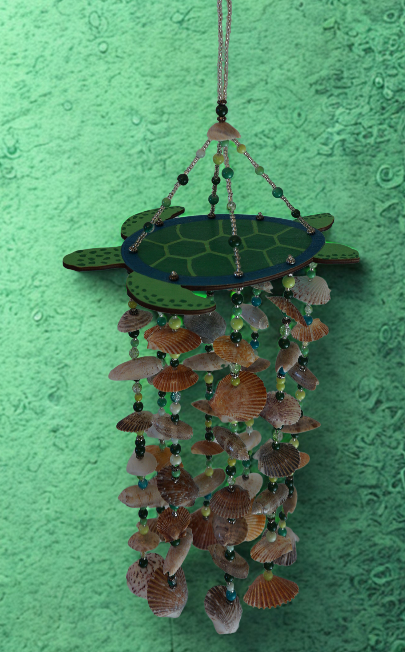 Decorative wind chime with turtle design and seashells on a green background