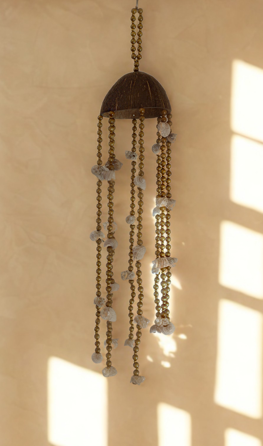 Coconut and shell wind chime hanging near a window on a beige wall