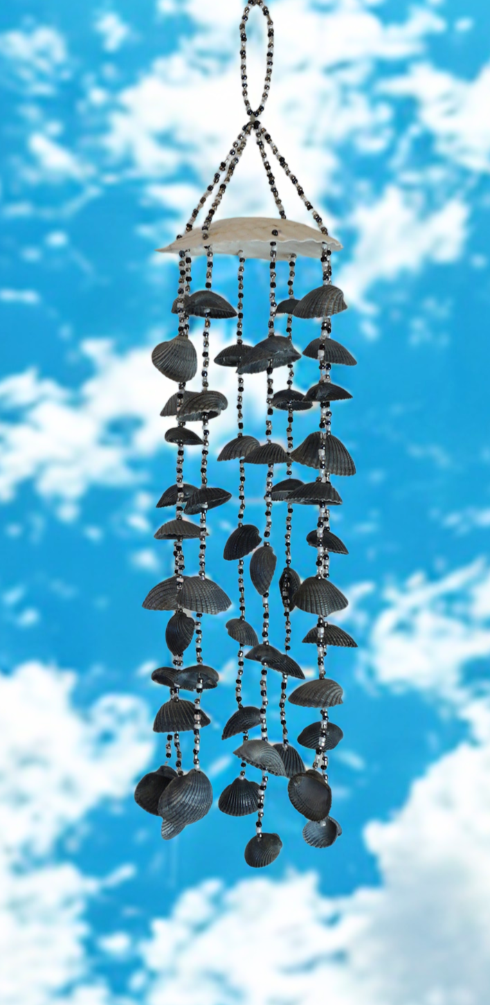 Wind chime with black shells against a blue sky with white clouds