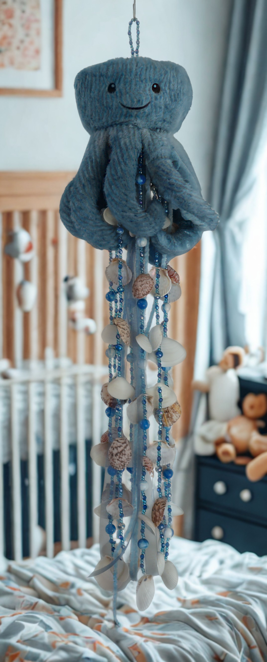 Decorative mobile with plush toy wind chime and beads hanging above a crib in a nursery.