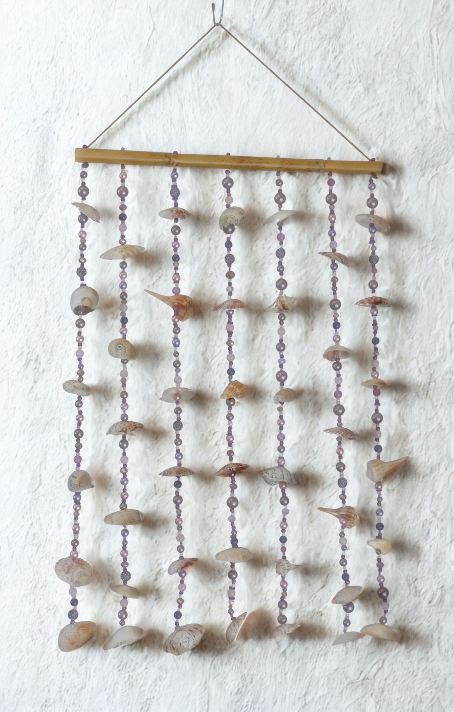 Decorative wall hanging with shell and bead elements on a white wall