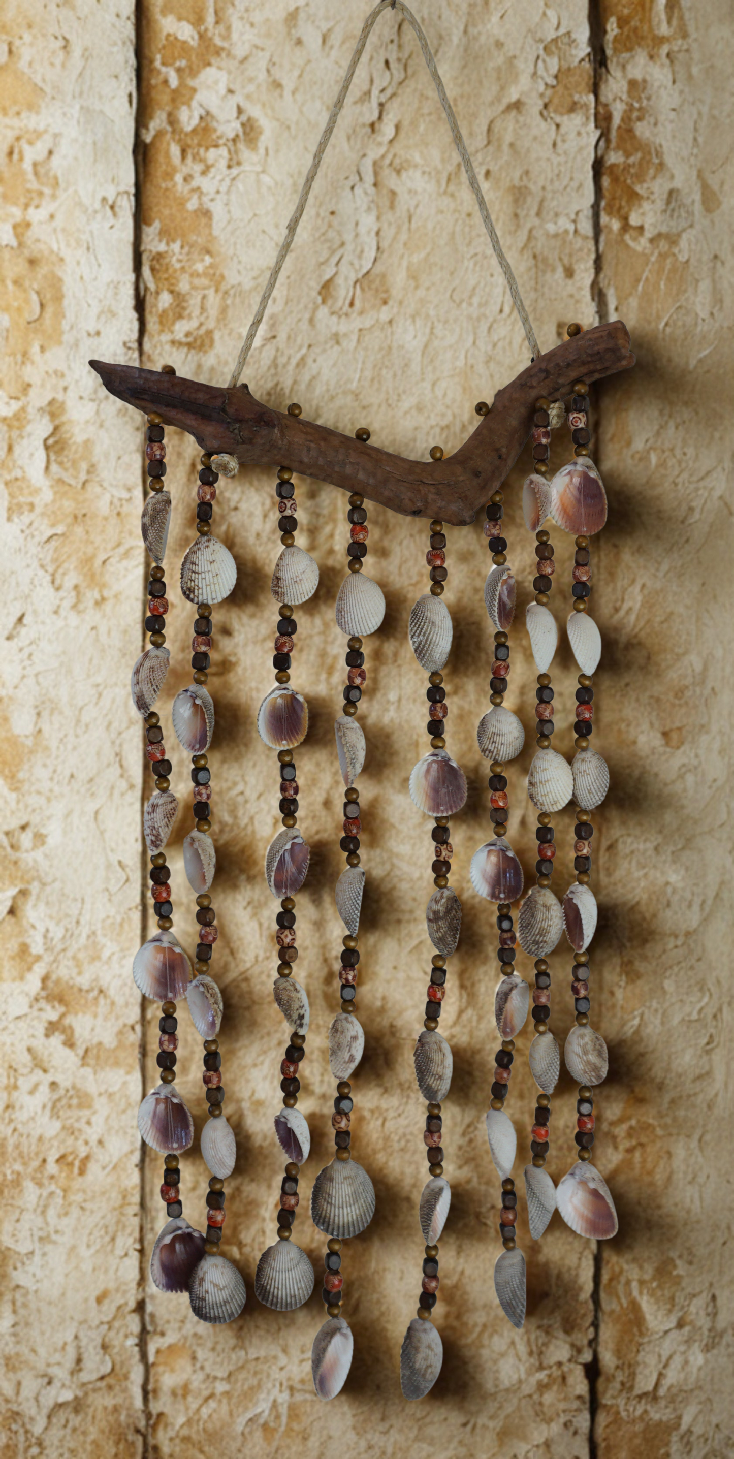 Decorative wall hanging with shells and beads and driftwood on a textured wall.