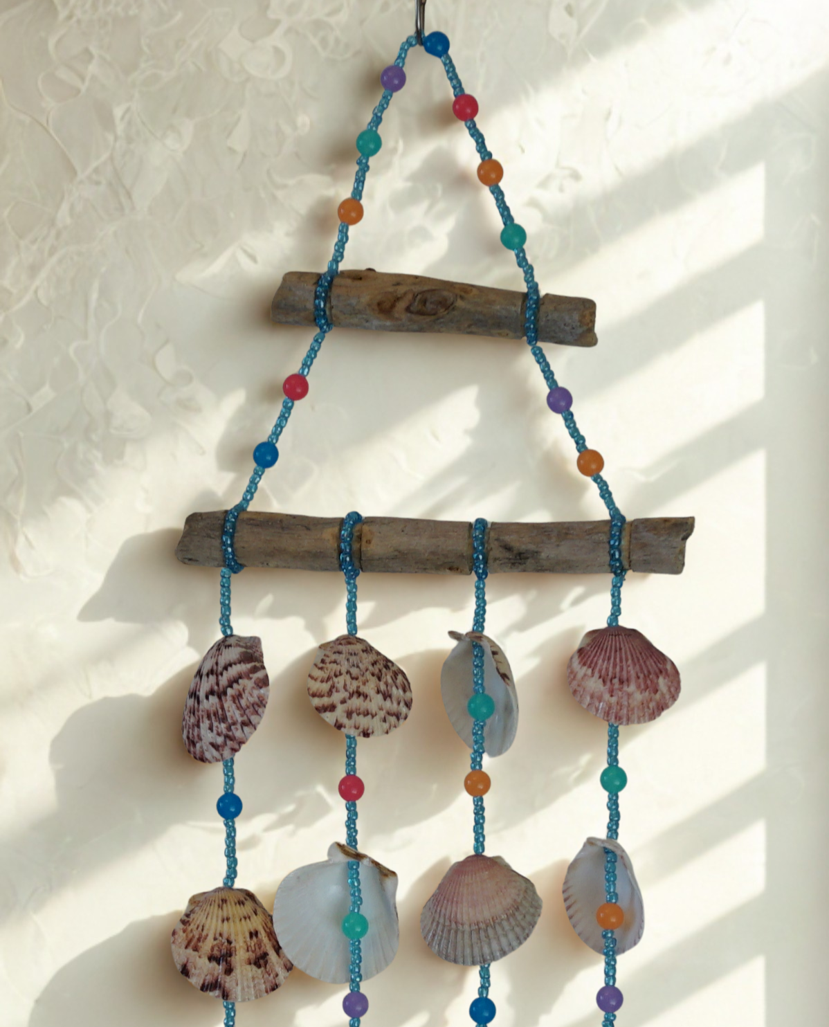 Decorative wall hanging with shells, beads, and driftwood on a light background
