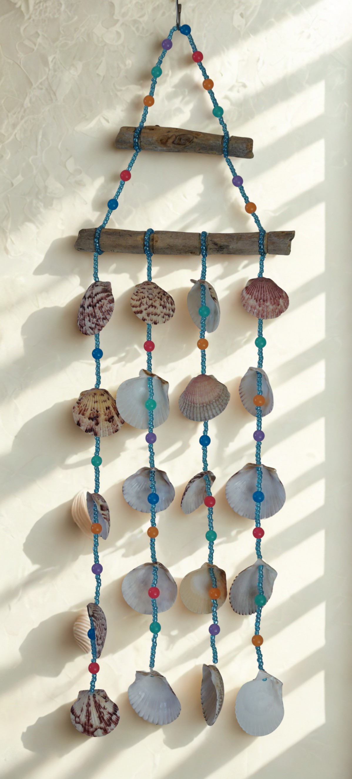 Decorative wall hanging with shells and beads on a white wall