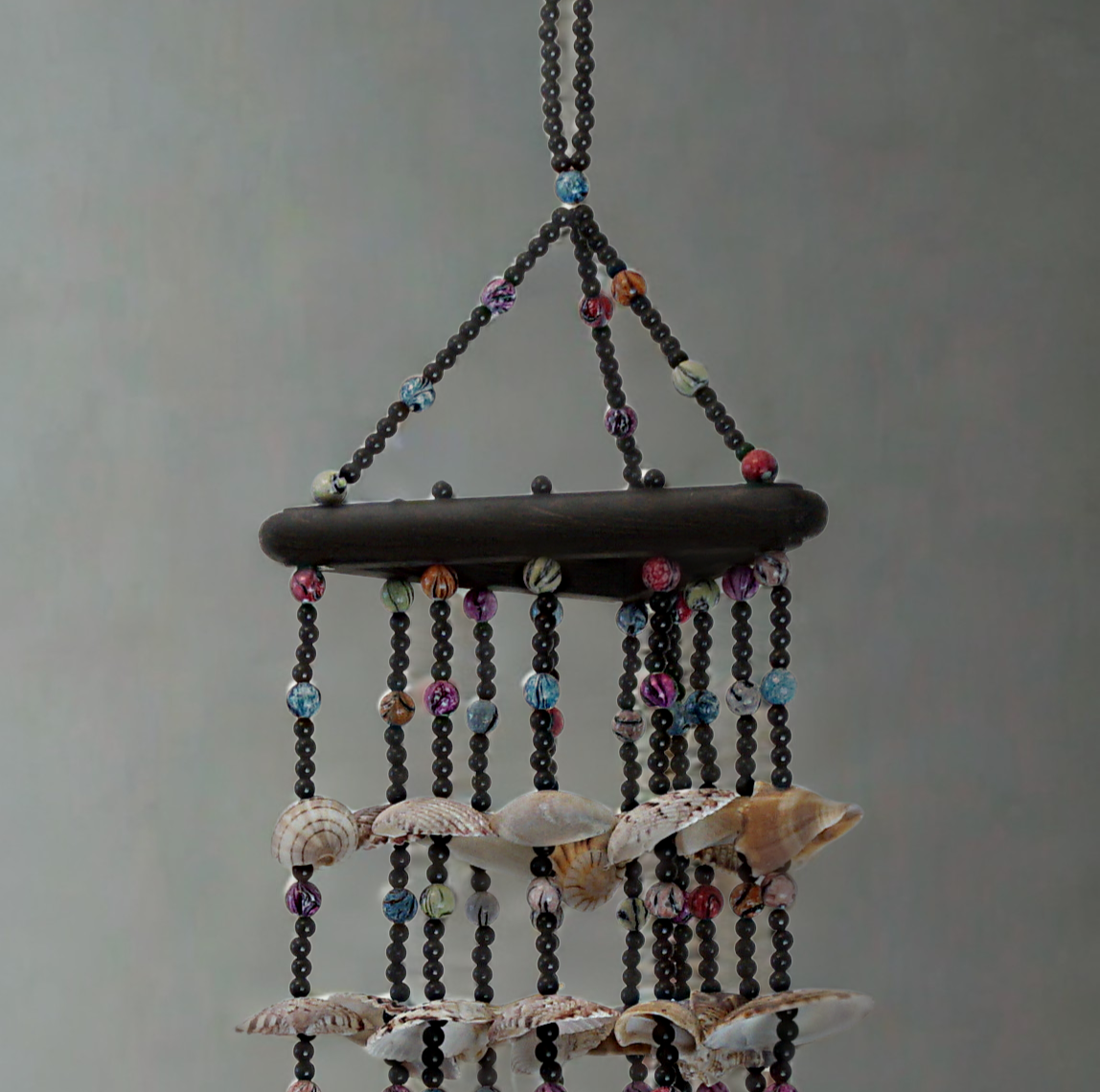 Decorative hanging wind chime with shells and beads on a plain background