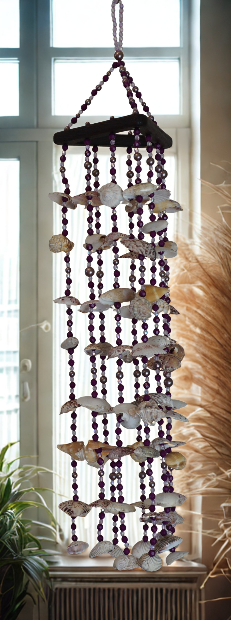 Decorative wind chime with seashells and beads in a room with a window and plant.