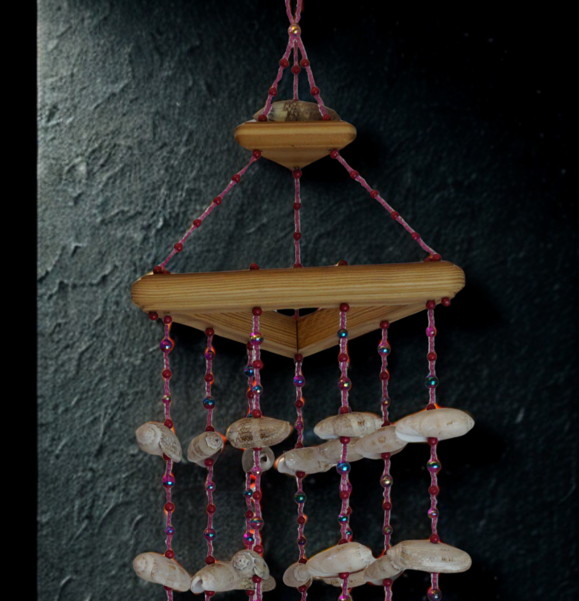Wooden hanging wind chime with shell decorations against a dark wall