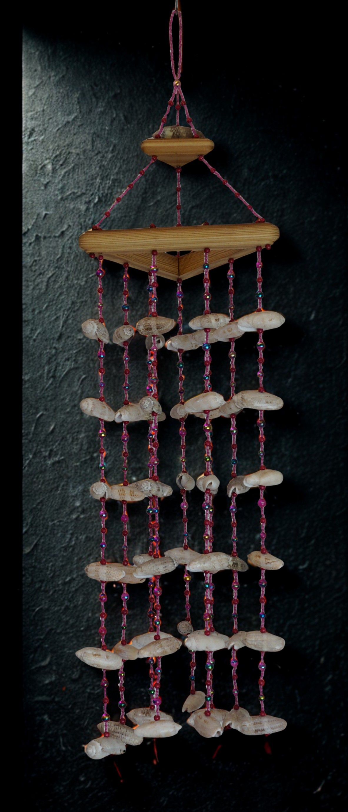 Decorative wind chime with wooden top and shell beads on a dark background