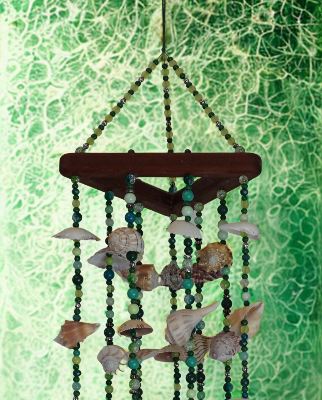 Decorative wind chime with seashells and beads against a green textured background