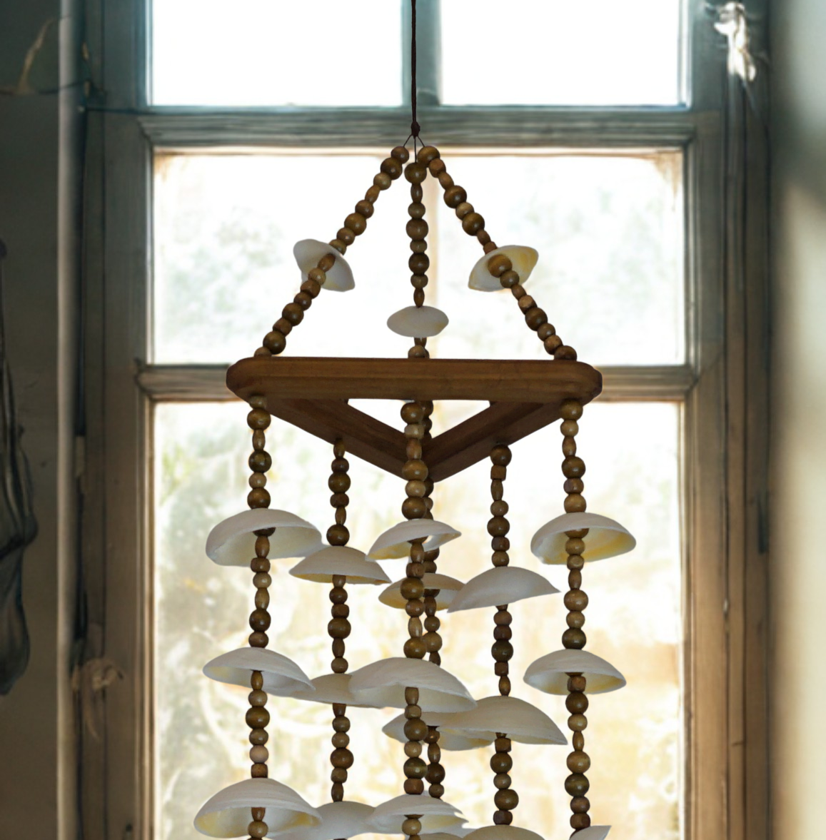Decorative wind chime with shell and bead design in front of a window