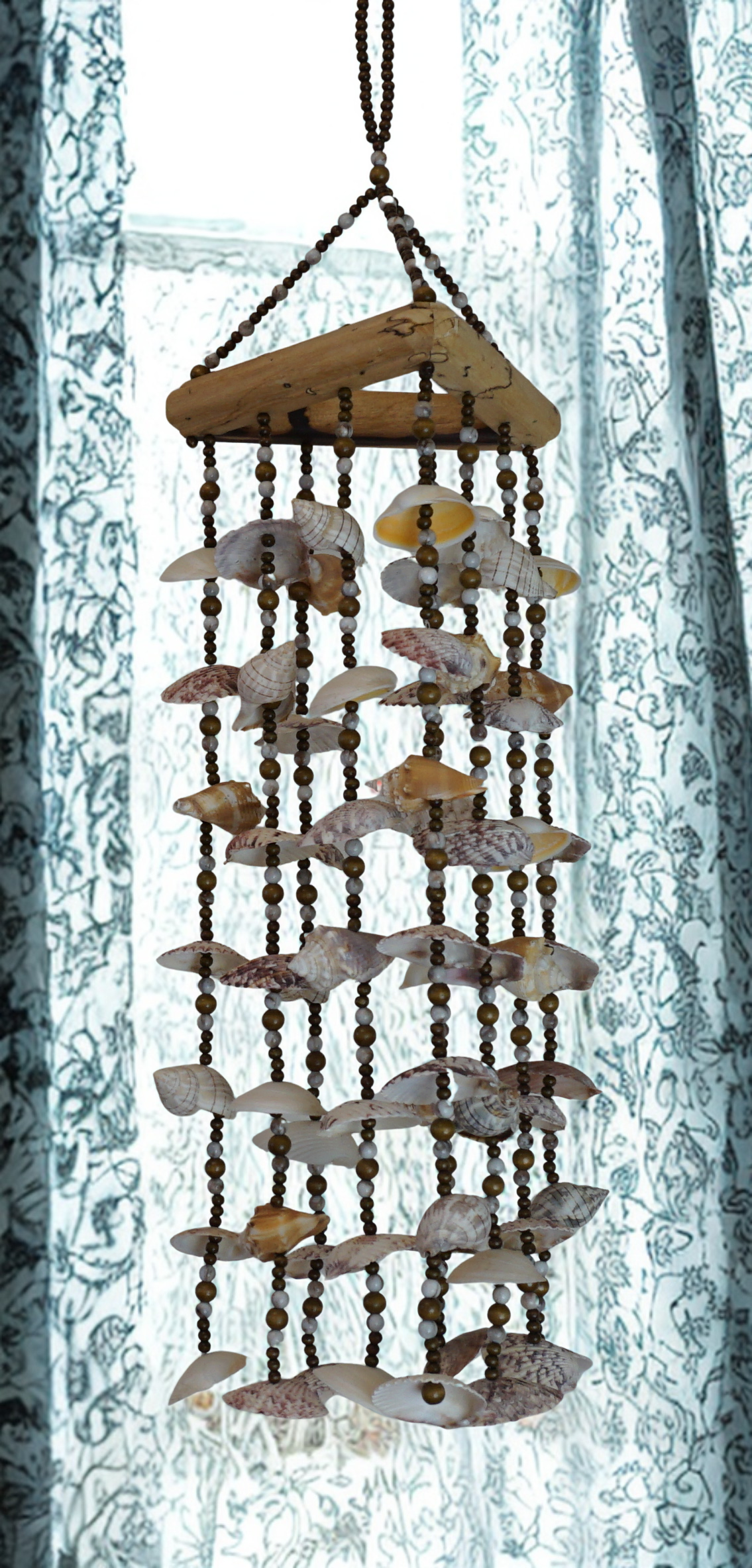Decorative shell wind chime hanging against a light curtain background