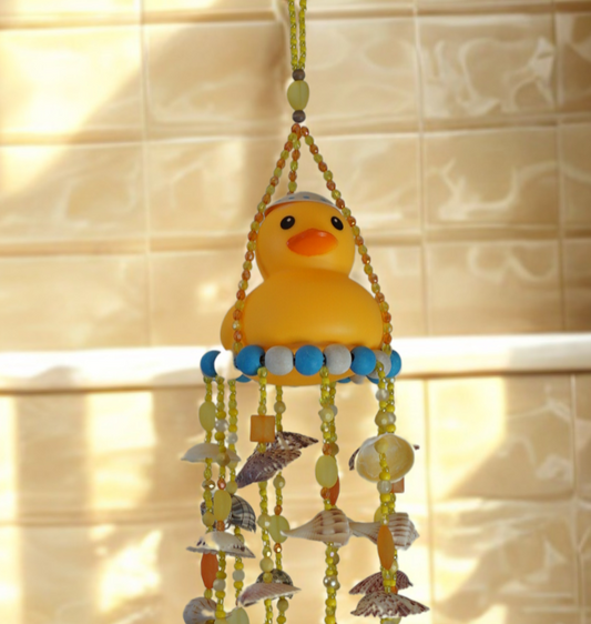 Decorative wind chime with a rubber duck on top with shells hanging against a tiled wall.
