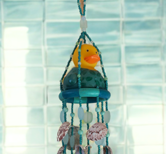 Decorative wind chime with a rubber duck and seashells against a tiled wall background