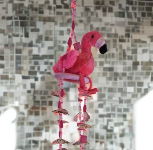 Pink flamingo wind chime with shells against a mosaic tile wall.