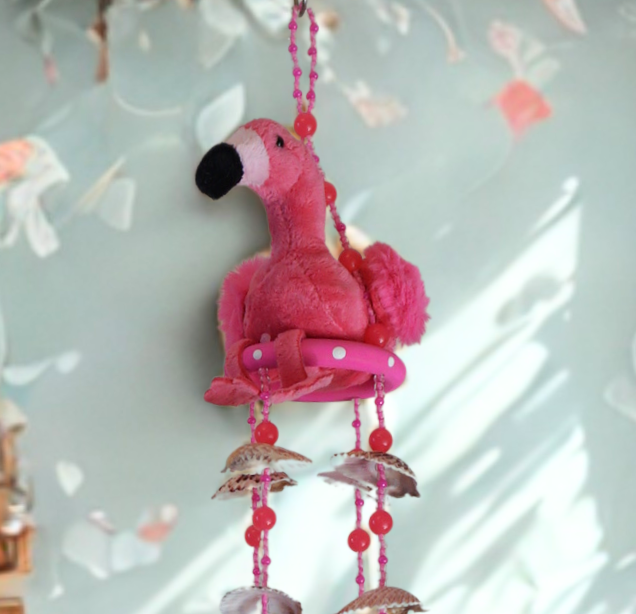 Pink flamingo plush toy wind chime with shells on a light background