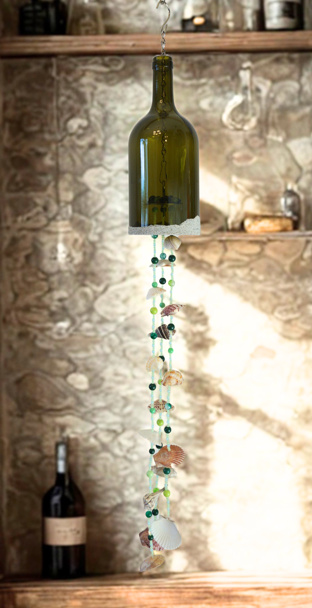 Decorative hanging bottle wind chime with beads and shells against a stone wall background