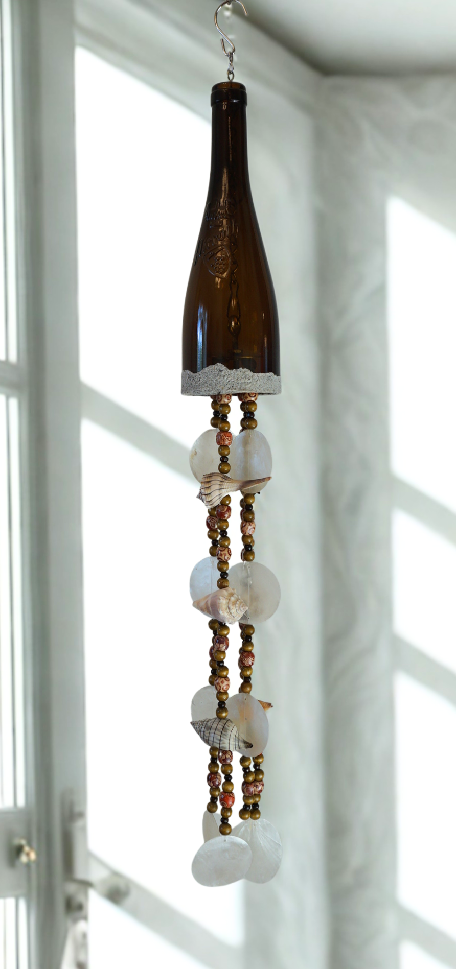 Decorative hanging bottle wind chime with beads and shells against a white window background