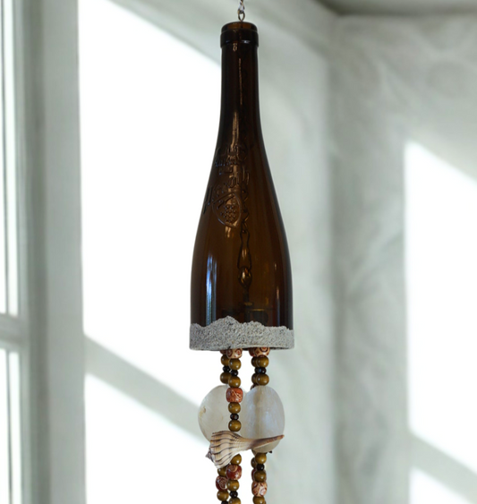 Decorative wind chime made from a wine bottle with beads and shells against a neutral background