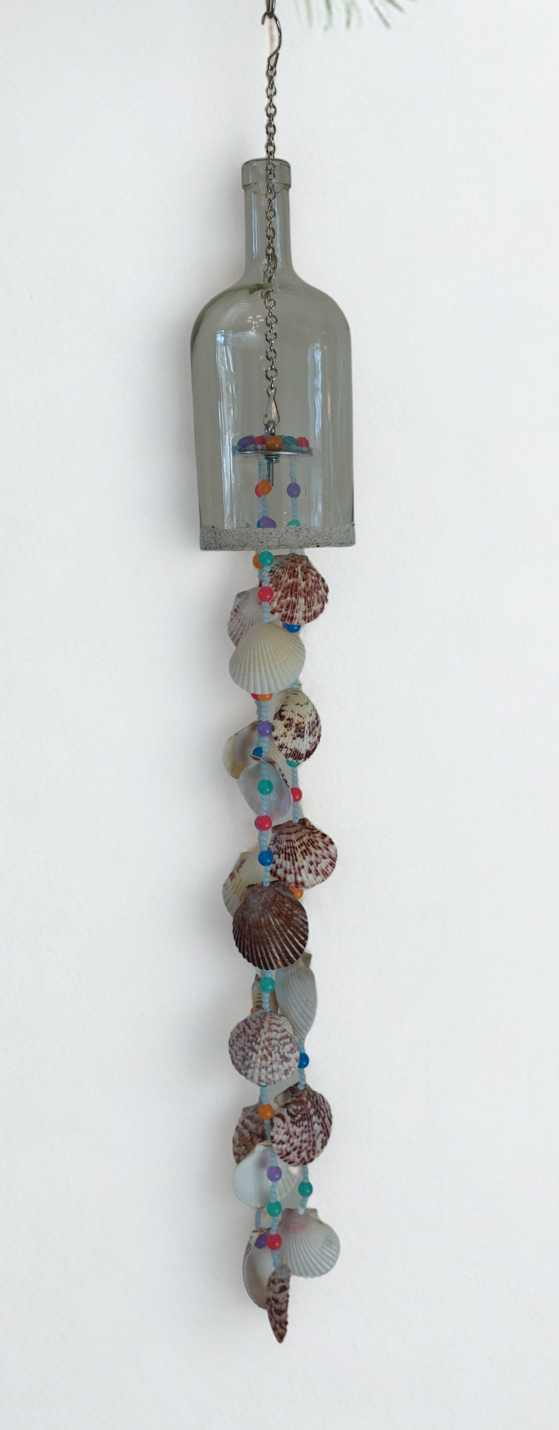 Decorative hanging bottle wind chime with seashells and beads on a white background