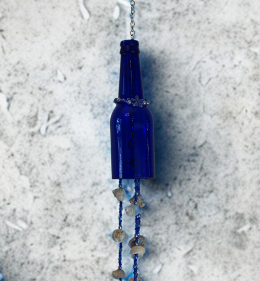 Blue glass bottle wind chime with decorative shell elements on a textured surface