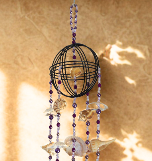 Decorative hanging wind chime with beads and seashells against a textured wall.