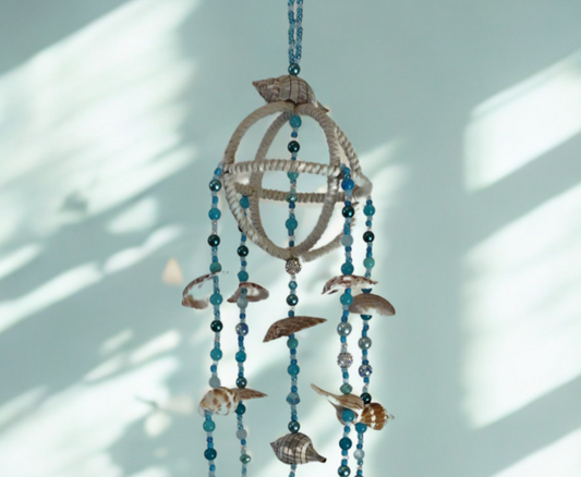 Decorative hanging wind chime with blue beads and shells against a light blue wall.