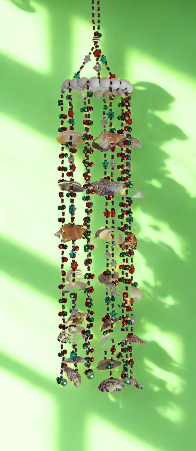 Decorative wind chime with colorful beads and shells on a green background