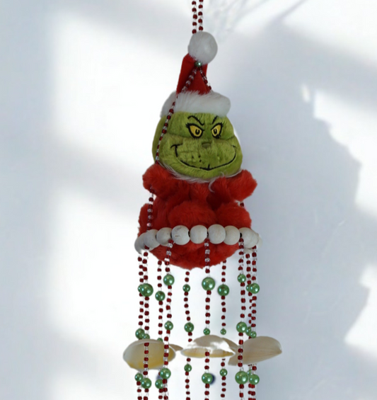 Decorative hanging wind chime with shells resembling a green character with a red outfit and Santa hat on a white background.