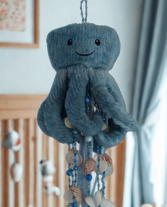 Decorative mobile with plush toy wind chime and beads hanging above a crib in a nursery.