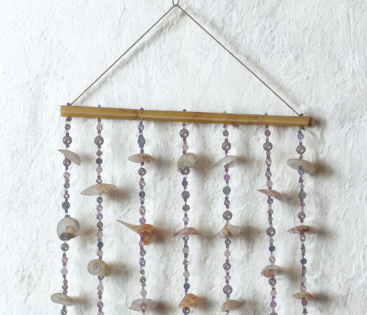 Decorative wall hanging with shell and bead elements on a white wall