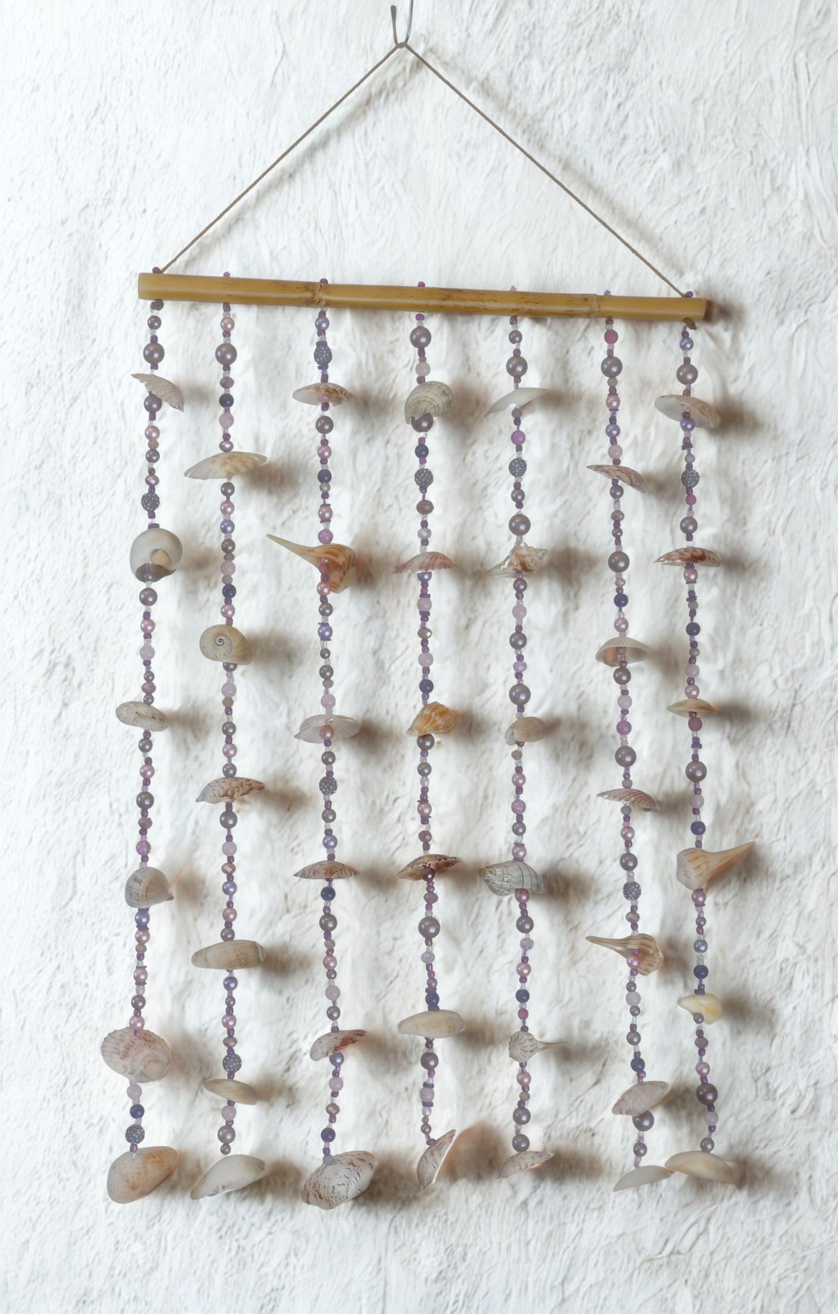 Decorative wall hanging with shell and bead elements on a white wall