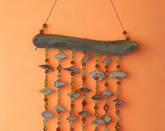 Driftwood wall hanging with shells and beads on an orange background