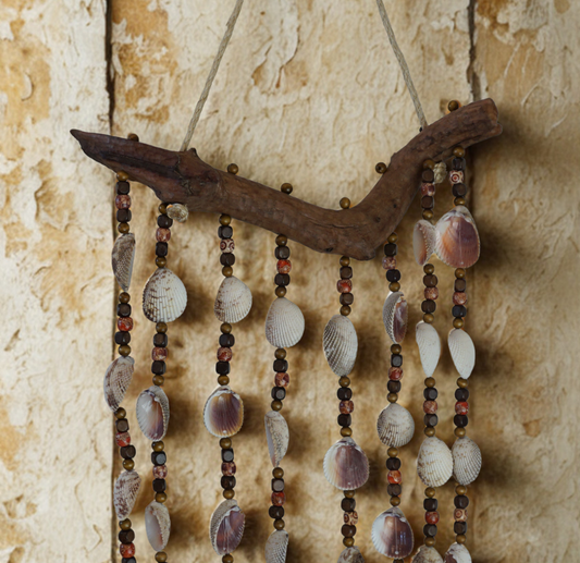 Decorative wall hanging with shells, beads and driftwood on a textured wall.